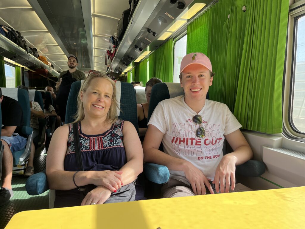 Amy and Cole seated across the table in a train. 